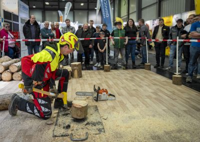 Arbeitssicherheitsvorführung der SVLFG, Mann in Sicherheitskleidung spaltet Holz mit einer Axt